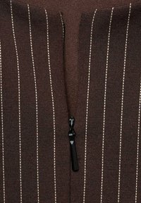 Hnědý zip-up oděv s vertikálními bílými proužky, s černým zipem a texturovaným vzorem tkaniny.