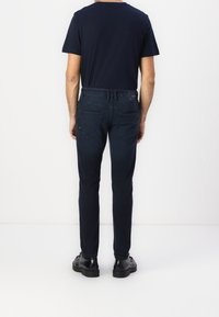 Dark blue jeans with a slim fit, two back pockets, and minimal stitching details, paired with a plain black t-shirt and black shoes.