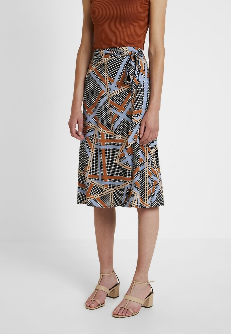 Haut côtelé marron associé à une jupe mi-longue à motifs géométriques en noir, bleu et marron, maintenue par un lien sur le côté à la taille.