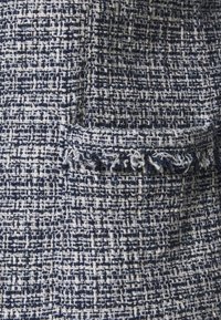 Granatowo-białe tkaniny o fakturze z wzorem tkanym, z małą kieszonką ozdobioną postrzępionymi krawędziami, dodającą dotykowego detalu.