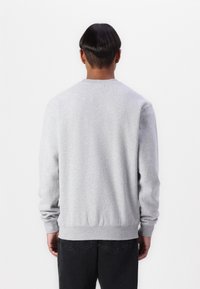 Sweat-shirt gris avec un col ras du cou et des poignets côtelés, présentant une texture lisse et une coupe légèrement ajustée à la taille.