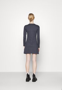 Mörkgrå långärmad klänning med utsvängd kjol och rund halsringning, tillverkad av mjukt tyg, bärs med svarta ankelskor.