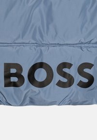 Svijetloplavi podstavljeni materijal s velikim crnim natpisom "BOSS". Glatka tekstura s blagim sjajem i horizontalnim šavom.