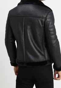 Schwarze Kunstlederjacke mit strukturierter Oberfläche, mit Pelzkragen und gerippten Schulterakzenten, entworfen mit einer taillierten Silhouette.