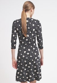 Zwarte jurk met wit bloemenpatroon, driekwart mouwen, aansluitende bodice, uitlopende rok, zachte stof, halflange snit.