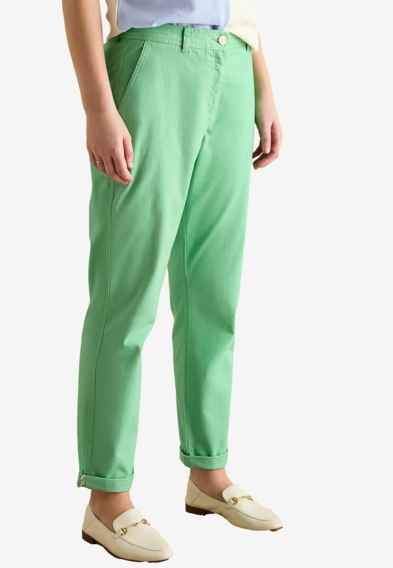 Rohelised puuvillased püksid sirge lõikega, küljetaskute, nööpkinnituse ja varrukakääristega. Kandmisel beežid loaferid.