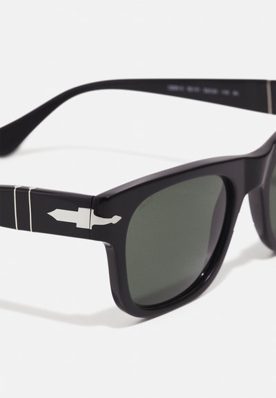 Sorte plastsolbriller med grønne linser, med et sølvfarget pennedesign på stangen og tynne hvite striper langs hengslet.