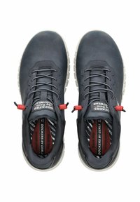 Chaussures en cuir gris foncé avec des accents rouges, des lacets robustes et une surface texturée. Elles sont dotées d'une semelle blanche et d'une doublure intérieure à motifs.