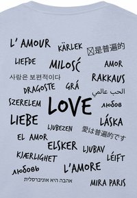 T-shirt azzurro chiaro con la parola "AMORE" e le sue traduzioni in diverse lingue, presentate in tipografia nera di varie dimensioni e stili.