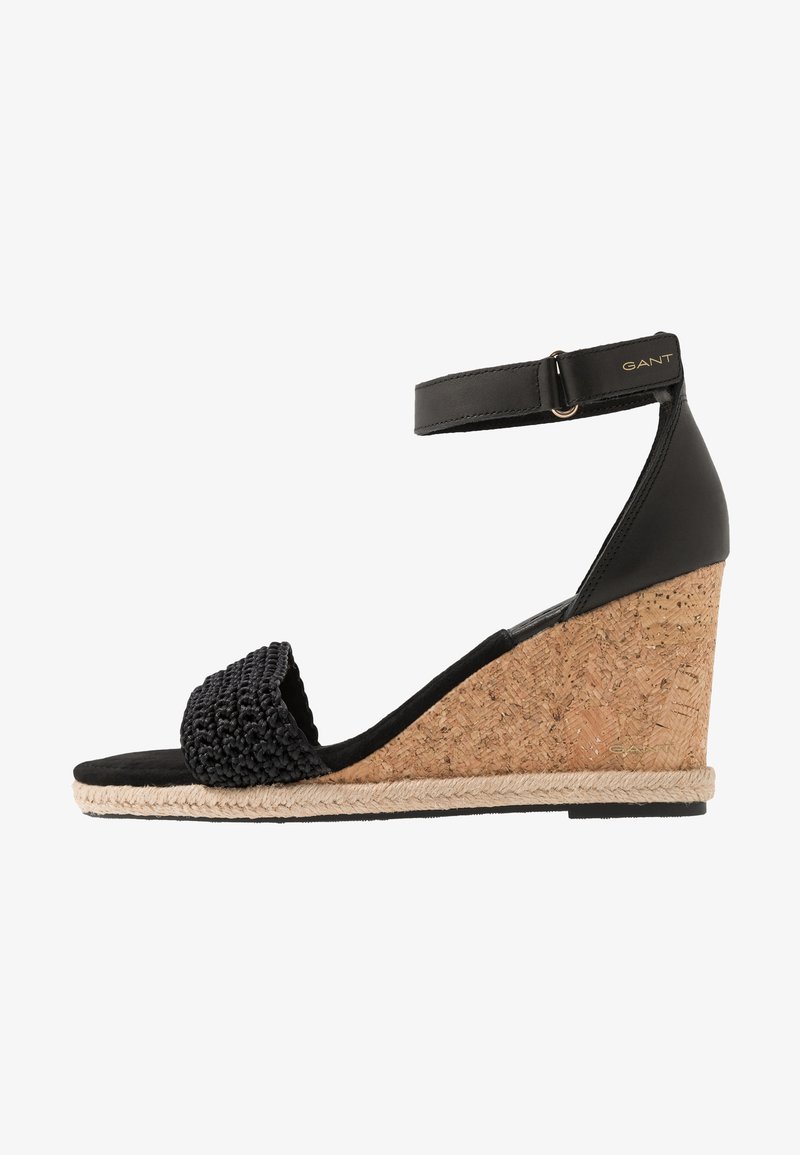 Black wedge sandals with cork heel, textured woven strap, ankle buckle closure, and contrast stitching along the base. Suitable for casual wear.