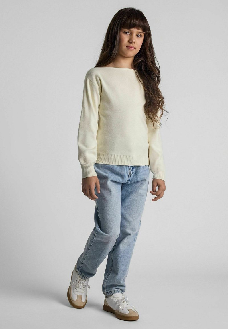 Pull à manches longues, col rond en crème clair, associé à un jean décontracté bleu clair et des baskets blanches avec des accents beige.