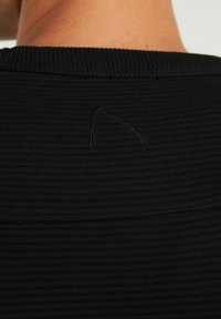 Schwarzer, strukturiert Stoff mit einem gerippten Design und einem kleinen, unfertigen Fadendetail am hinteren Halsausschnitt.