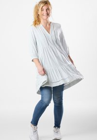 Gestreifte, knielange Tunika in Hellblau und Weiß, mit V-Ausschnitt, 3/4-Ärmeln und fließendem Saum. Kombiniert mit Jeans und Sneakers.