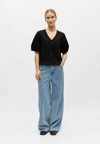 Haut noir à manches courtes avec un col en V et un seul bouton, associé à un jean larges jambes bleu clair et des chaussures noires.