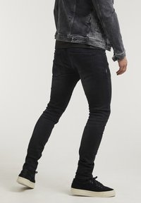Svarta slim-fit jeans i denim med en mörk tvätt, bakfickor med dekorativ sömnad, kombinerade med svarta sneakers och en grå denimjacka.
