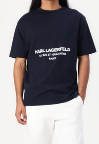 Navy blue bawełniany t-shirt z wyraźnym białym napisem "KARL LAGERFELD 21 RUE ST-GUILLAUME PARIS." Luźny krój z krótkimi rękawami.