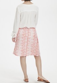 Blusa bianca a maniche lunghe abbinata a una gonna rosa a fantasia, lunga fino al ginocchio, con motivo a stampa rettile. Sandali piatti marroni.