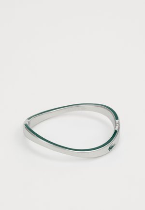 Bracelet en argent au design fluide, avec un bandeau intérieur vert et un petit accent logo. Surface métallique lisse avec une forme moderne.