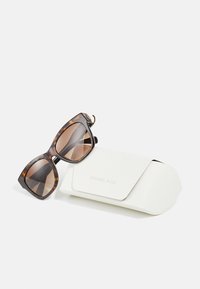 Hnědé želvovinové sluneční brýle s odvádným, úhlovým designem, doplněné o bílý pouzdro s embossovaným nápisem "MICHAEL KORS."