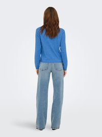 Pull en maille bleu à manches longues, associé à un jean large lavé clair. La tenue présente un design décontracté et une texture douce.