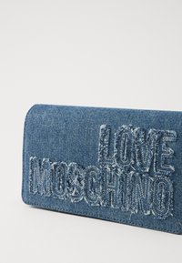 Portafoglio in denim con texture invecchiata, lettering «LOVE MOSCHINO» in rilievo e forma rettangolare. Colore blu con una finitura morbida.