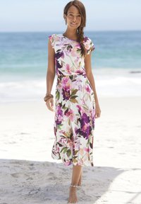 Maxikleid mit lila und rosa Blumen auf weißem Hintergrund. Kurze Ärmel, tailliert, fließender Rock; getragen mit einem Armband.