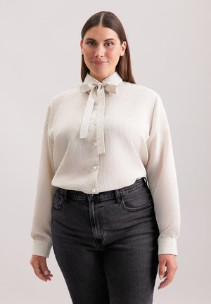 Cremefarbene gestreifte Bluse mit einer Schleifenkragen, durchgehender Knopfleiste, langen Ärmeln und kombiniert mit hoch sitzenden dunkelgrauen Jeans.