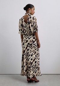 Vestido maxi de estampado de leopardo en tejido beige claro, con un corte en la espalda, mangas sueltas y una silueta fluida. Acentuado con tacones con tiras.