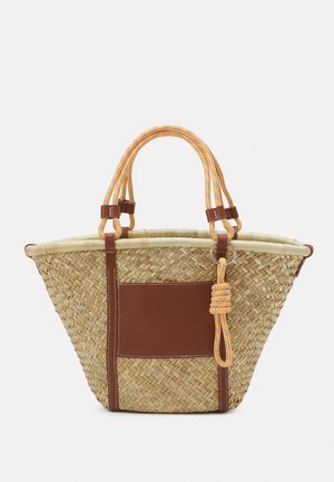 Sac fourre-tout en paille tissée avec des accents en cuir marron, des poignées orange et à motifs, et une grande poche à panneau marron sur un côté.