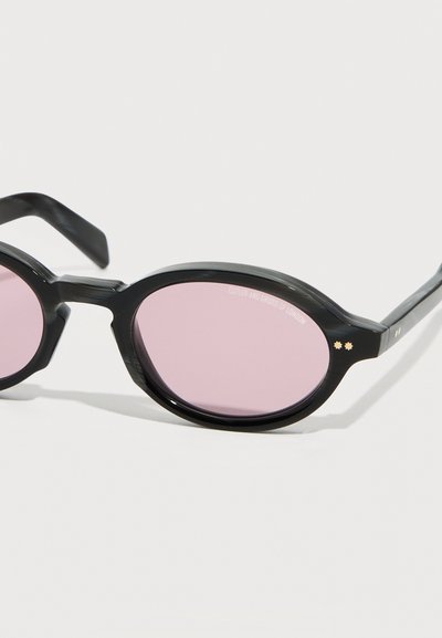 Στρογγυλά μαύρα γυαλιά ηλίου με ροζ φακούς και δύο μικρές χρυσές αστέρια στη γωνία του σκελετού.