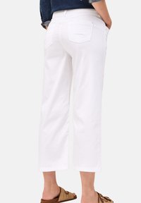 Pantalones recortados blancos de algodón, con un corte clásico, dos bolsillos traseros y una textura suave. Combinados con sandalias de tiras marrones.