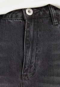 Black denim jeans featuring a metal button closure and stitched detailing, focusing on the waistband and textured fabric.