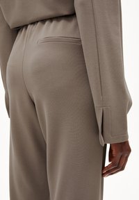 Pantalon en jersey gris avec une coupe décontractée, taille élastique et une poche arrière unique, avec une texture lisse et un détail de revers ajusté.