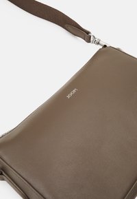 Borsa a tracolla in pelle marrone con una texture liscia, dotata di accessori in metallo argentato e del logo "JOOP!" impresso nella parte frontale.