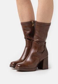 Bottines en cuir marron avec une finition lisse, dotées d'une fermeture éclair, d'un talon carré et d'un design légèrement affaissé.