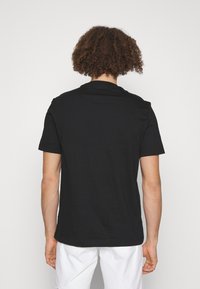 Svart kortärmad bomullströja med rundad halsringning och avslappnad passform, visas från baksidan, kombinerad med vita shorts.