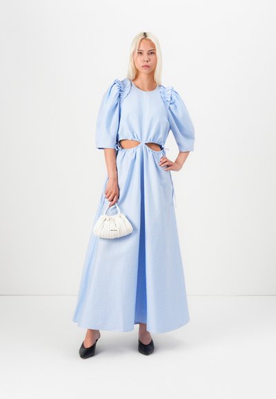 Rochie lungă, de culoare bleu deschis, cu mâneci bufante și tăieturi laterale, strânsă în talie; asociată cu o geantă plisată albă și pantofi negri.