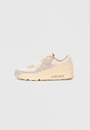Sapatilhas Nike Air Max em bege e creme com sola de amortecimento de ar visível e parte superior em camurça e malha mistas, exibidas sobre um fundo simples.