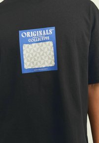 Sort bomulds t-shirt med et blåt rektangulært grafik med teksten "ORIGINALS COLLECTIVE" og et tekstureret geometrisk mønster i grå.
