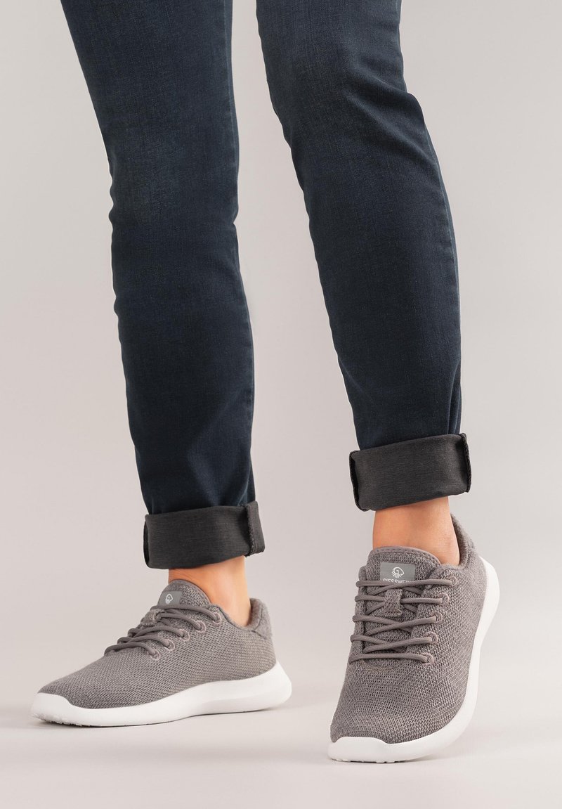 Szare sportowe buty z dzianiny z białymi podeszwami, sznurowane, z zaokrąglonym noskiem, w zestawieniu z podwiniętymi ciemnymi jeansami.