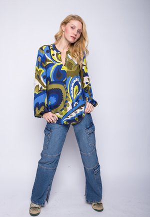 Multikleurige blouse met blauwe, groene en gele paisleypatronen, gecombineerd met losse denim cargobroeken met zakken en een rechte pijp.