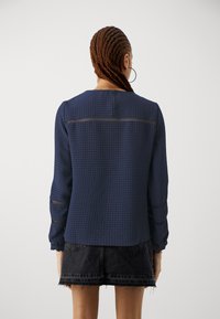 Navy blue textured blouse with long sleeves, round neckline, and sheer striped details on sleeves. Paired with a high-waisted black denim skirt.