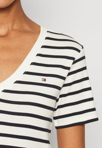 T-shirt a righe a maniche corte con scollatura a V in bianco e blu navy, dotato di un piccolo logo sul lato sinistro del petto e una morbida texture di cotone.