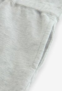 Ljusgrått, mjukt tyg i närbild av ett plagg som har en subtil textur och en sidoficka designad i materialet.