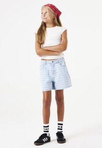 Shorts en denim bleu clair avec un motif subtil, associés à un haut ajusté blanc et des baskets noires avec des accents blancs. Bandana rouge dans les cheveux.