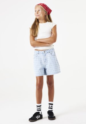 Shorts en denim bleu clair avec un motif subtil, associés à un haut ajusté blanc et des baskets noires avec des accents blancs. Bandana rouge dans les cheveux.
