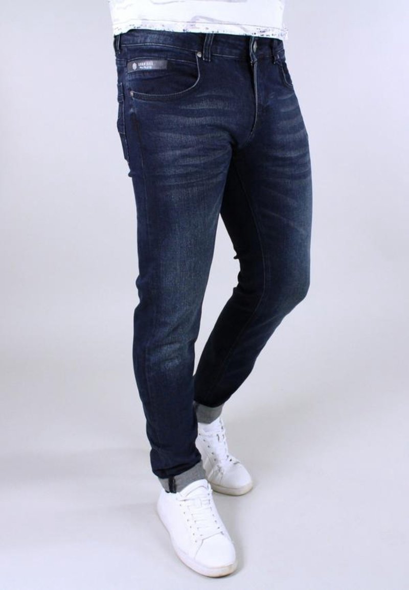 Dark blue jeans with a slim fit, featuring subtle fading and whiskering on the front. Paired with white sneakers.