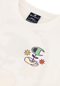 Witte katoenen T-shirt met een kleurrafische afbeelding van een hand die een plant vasthoudt met een gestileerd blad, omringd door twee glimlachende sterren.