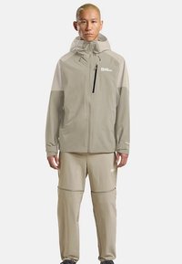 Leichte, beige Outdoorjacke mit Kapuze und Reißverschlusstaschen, kombiniert mit passenden beigen Hosen mit Reißverschlussdesign.