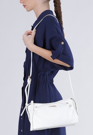 Donna con capelli intrecciati che indossa un vestito blu navy, con una borsa a tracolla in pelle bianca con dettagli in oro.